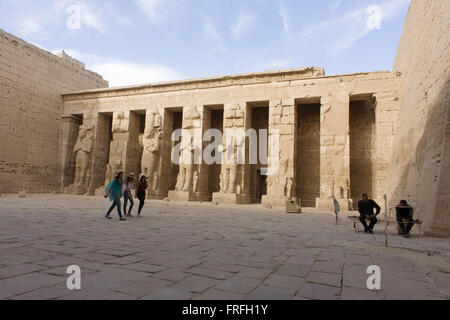 Women tourists walk past tall Ramessid columns in the peristyle court at the ancient Egyptian site of Medinet Habu (1194-1163BC), the Mortuary Temple of Ramesses III in Luxor, Nile Valley, Egypt. Medinet Habu is an important New Kingdom period structure in the West Bank of Luxor in Egypt. Aside from its size and architectural and artistic importance, the temple is probably best known as the source of inscribed reliefs depicting the advent and defeat of the Sea Peoples during the reign of Ramesses III. Stock Photo