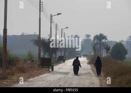 Local women walk along a hot road towards Qurna, a village on the West Bank of Luxor, Nile Valley, Egypt. In Egypt, sugar cane juice is called aseer asab and is by far the most popular drink served by almost all fruit juice vendors, who are abundant in most cities. It is sold by roadside vendors, where the juice is squeezed fresh when ordered. Raw sugar cane juice can be a health risk to drinkers due to the unhygienic conditions under which it is prepared. There are some diseases that can be transmitted by raw sugar-cane like Leptospirosis Stock Photo