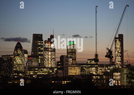 The sun is setting on the City of London and the lights are on, seen from Hackney, East London.
