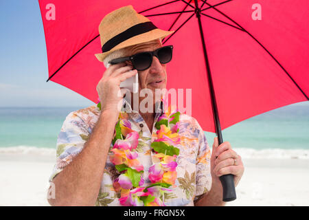 Senior man holding umbrella while talking on phone Stock Photo