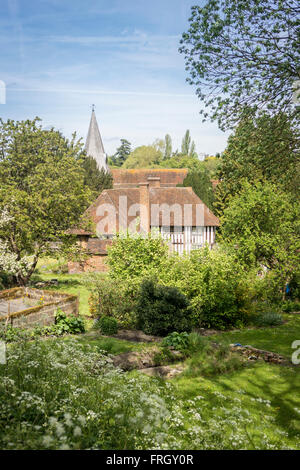 View across a garden of a half-timbered cottage with the church spire behind it Stock Photo