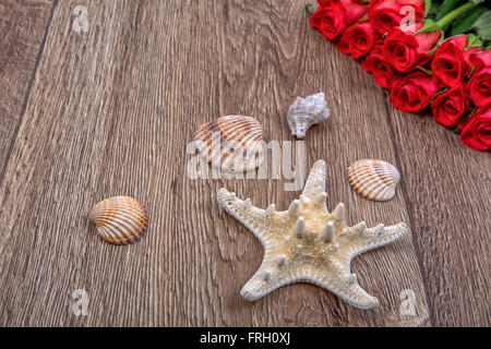 White starfish, shells and red roses on a wooden background Stock Photo