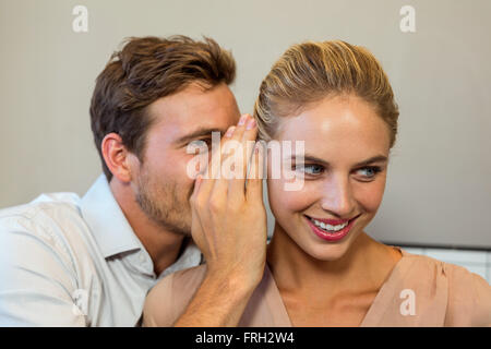 Man whispering to female colleague in office Stock Photo
