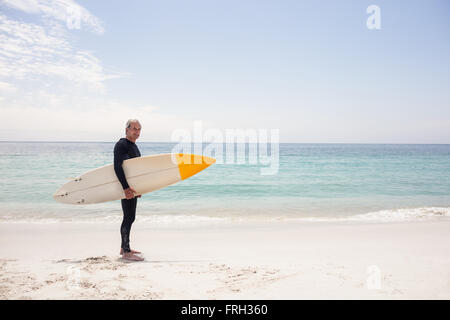 Portrait of senior man in wetsuit holding a surfboard Stock Photo