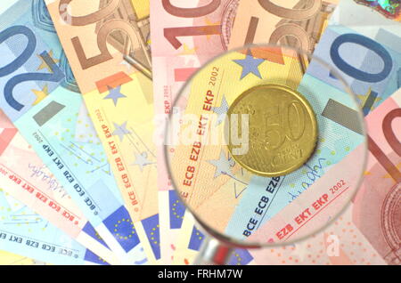 coin on euro banknotes under magnifying glass Stock Photo