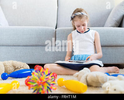 It's time to clean up your toys! Little girl playing with tablet pc, don't want to do the cleaning. Stock Photo