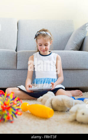 It's time to clean up your toys! Little girl playing with tablet pc, don't want to do the cleaning. Stock Photo