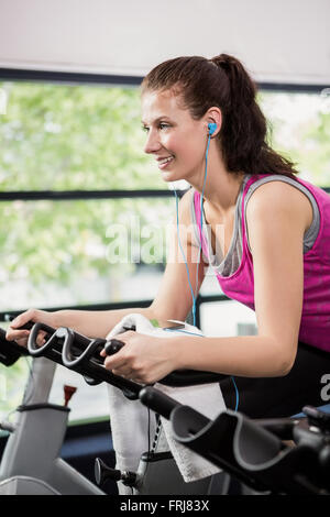 Woman listening to music while working out on exercise bike Stock Photo