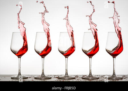Red wine splashing from five wine glasses Stock Photo