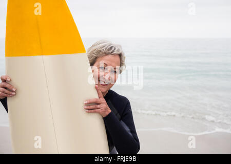 Senior woman in wetsuit holding a surfboard on the beach Stock Photo