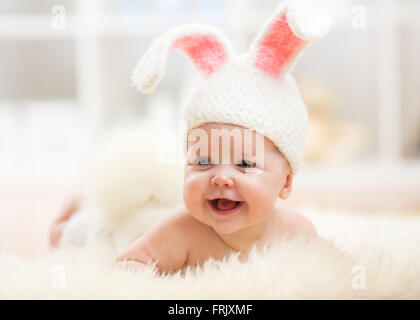 Smiling baby girl in rabbit costume lying on fur in nursery Stock Photo