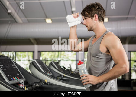 Tiered man standing on treadmill with water bottle Stock Photo