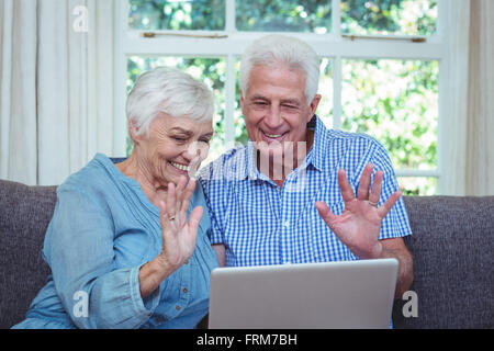 Smiling senior couple waving hand while using laptop Stock Photo
