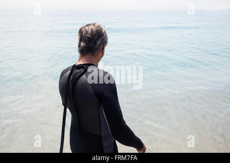 Rear view of senior man in wetsuit looking at sea Stock Photo