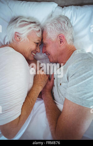 Senior couple touching head while holding hands on bed Stock Photo