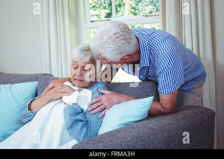 Senior man talking to ill wife sitting on sofa Stock Photo