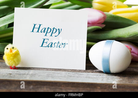 Happy Easter greeting card surrounded by Easter egg, flowers and watchful chick. Stock Photo