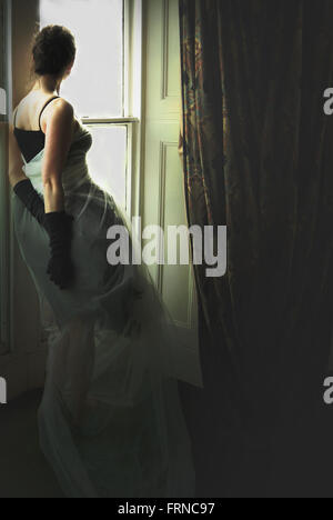 young elegant woman standing by the window in old house Stock Photo