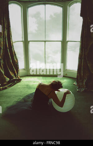 young woman sitting on the floor in an old house holding a big ball Stock Photo