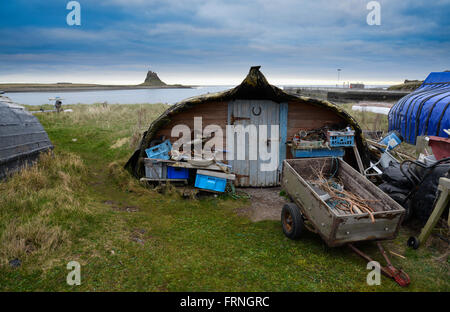 Lindisfarne Castle and the herring boat sheds which surround the harbour still in use today by fishermen for work and storage Stock Photo