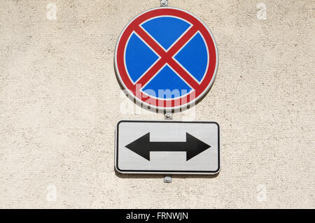 Modern road reflecting  signs "The Parking Is Forbidden" and "the Arrow on two directions" hangs on a  yellow concrete wall. Stock Photo