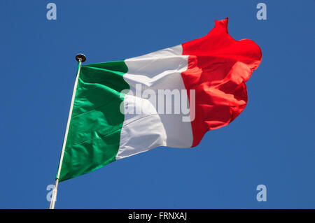 Italian flag fluttering in a brisk breeze against a bright blue sky. Stock Photo