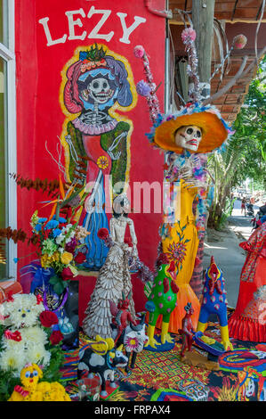 Dia de Los Muertos Day of the Dead figures of La Catrina w/ colorful mural + crafts displayed outside shop in Sayulita, Mexico. Stock Photo