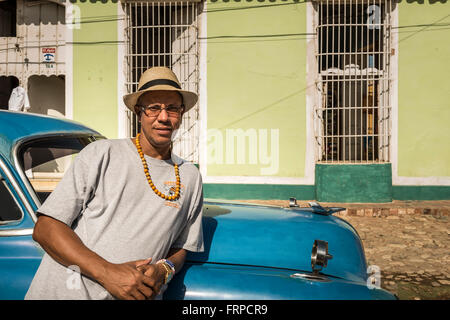 A Cuban man leaning on an old blue 1950's Chevrolet. Trinidad, Cuba Stock Photo