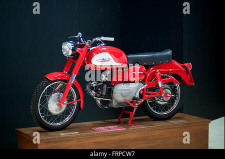 Single old fashioned red and white Harley Davidson- Aermacchi motorcycle on wooden display stand in front of black background Stock Photo