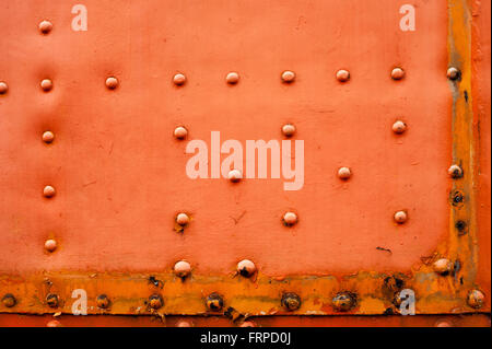Old faded red metal background with a random pattern of studs, corrosion and rust in a full frame view Stock Photo