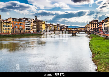 historic buildings overlooking the Arno river that flows peacefully under the arches of the ancient bridge of Florence on a bright winter day Stock Photo