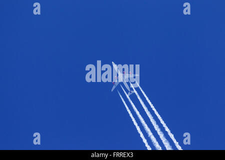 Engine exhaust contrails - cirrus aviaticus - forming behind four-engine Airbus A340 plane against blue sky Stock Photo