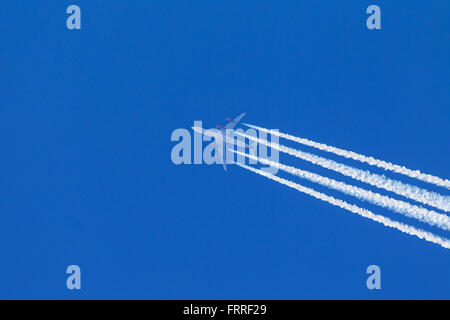 Engine exhaust contrails - cirrus aviaticus - forming behind four-engine Airbus A340 plane against blue sky Stock Photo