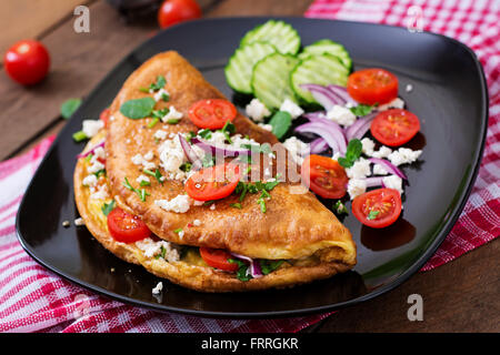 Omelet with tomatoes, parsley and feta cheese on black plate. Stock Photo
