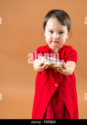 Pretty little girl holding donuts at brown background in studio Stock Photo