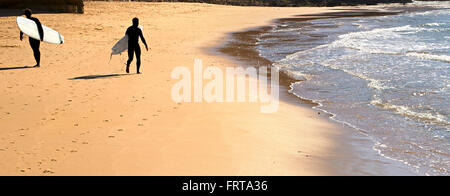 Surfers walking on the beach in the bright sunny day Stock Photo