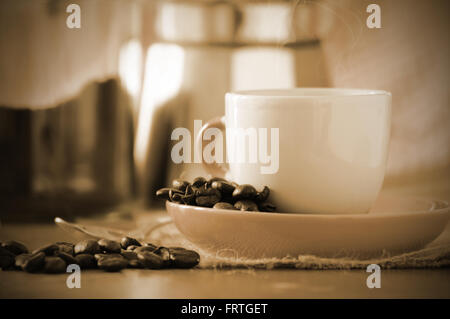 Cup of coffee next to some coffee beans on a table in a rustic kitchen. Empty copy space for editor's text. Stock Photo