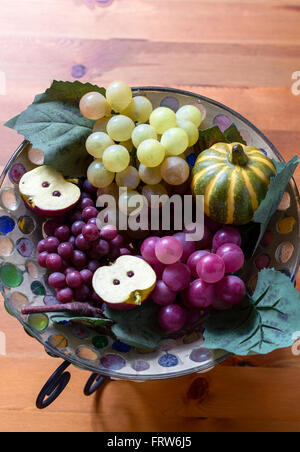 Close-up of artificial grape bunches, apple and pumpkin in glass plate on wooden table. From above Stock Photo