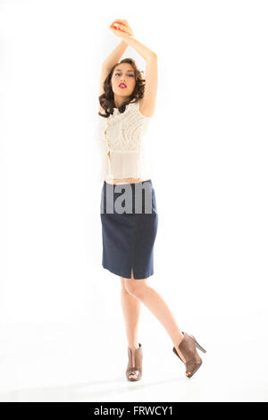 Beautiful young woman in white blouse and blue denim skirt, full length in brown heels, arms raised over head, hands clasped. Stock Photo