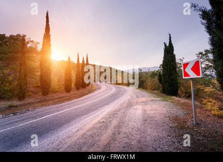 Beautiful asphalt road with road sign in mountains at sunset in summer. Stock Photo