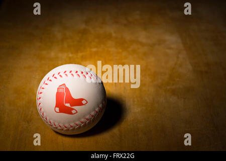 White rubber baseball with the Boston Red Sox logo printed on the side along with red stitching resting on a wooden table Stock Photo