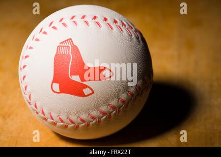 White rubber baseball with the Boston Red Sox logo printed on the side along with red stitching resting on a wooden table Stock Photo