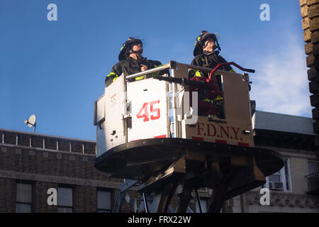 Two Firemen from Engine 45 in Manhattan being lifted inside an aerial platform ladder truck's bucket to the side of a building Stock Photo