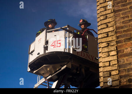 Two Firemen from Engine 45 in Manhattan being lifted inside an aerial platform ladder truck's bucket to the side of a building Stock Photo