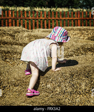 Little girl is climbing up on the haystack. Leisure activity. Stock Photo