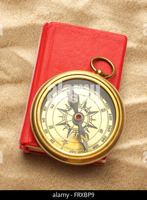 Red closed book with retro compass on sand Stock Photo