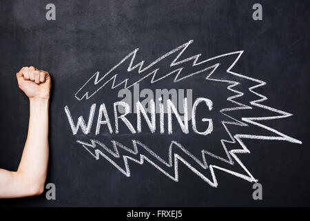 Hand showing fist near warning drawn on blackboard by chalk