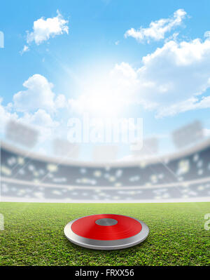 A discus in a generic sports  stadium resting on a marked green grass pitch in the daytime under a blue sky Stock Photo