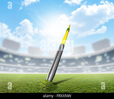 A javelin pegged into the turf of a generic sports  stadium with a marked green grass pitch in the daytime under a blue sky Stock Photo