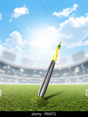 A javelin pegged into the turf of a generic sports  stadium with a marked green grass pitch in the daytime under a blue sky Stock Photo